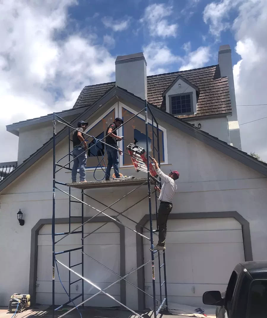 Three workers replacing a window on a garage addition