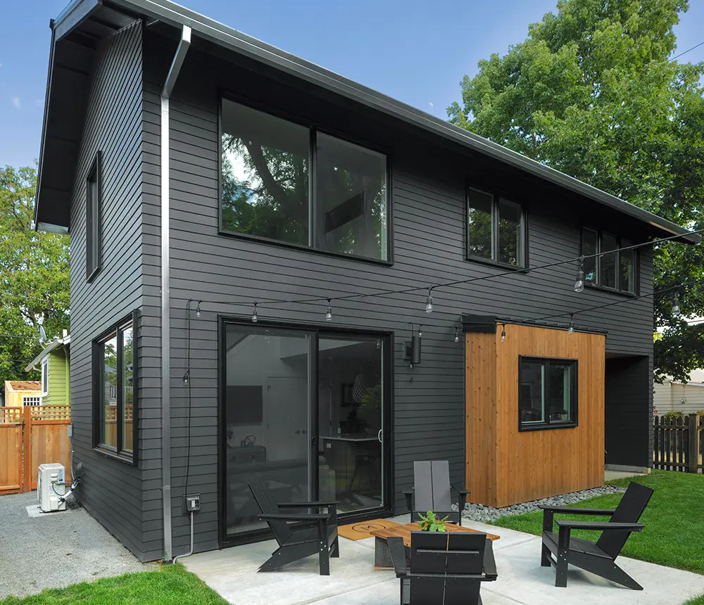A two-story home painted black with a concrete patio