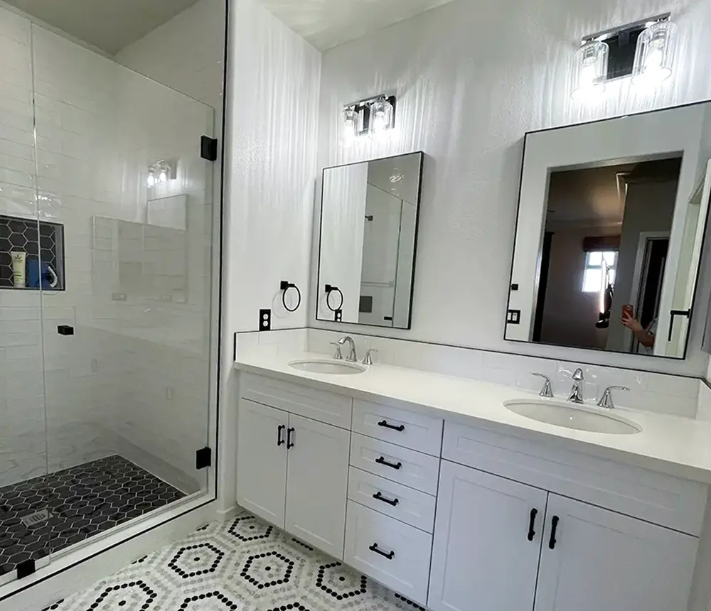 A bathroom with a double vanity with black pulls and two rectangular mirrors in a space with beautiful tile flooring