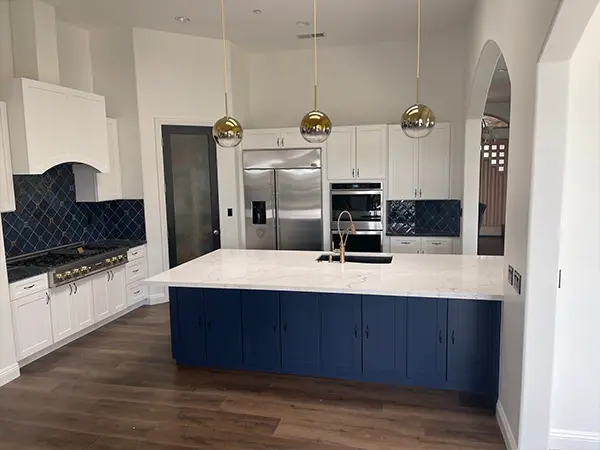 Wood flooring in a kitchen with navy blue and white kitchen cabinets and pendant lights