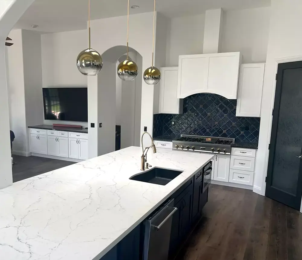 A beautiful quartz countertop on a large island and a dark blue tile backsplash in a kitchen with pendant lights and LVP flooring